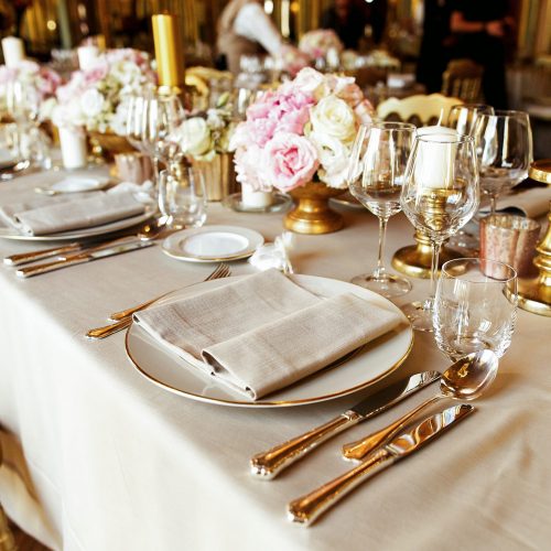 Shiny glassware and cutlery stand on the dinner table decorated with golden vases